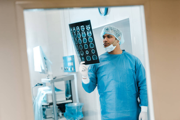 gutaussehender Arzt in Uniform und medizinischer Mütze schaut sich Röntgenbild in Klinik an  - Foto, Bild