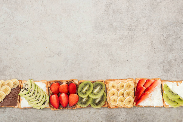 Top view of toasts with cut fruits, berries and peanuts on textured surface - 写真・画像