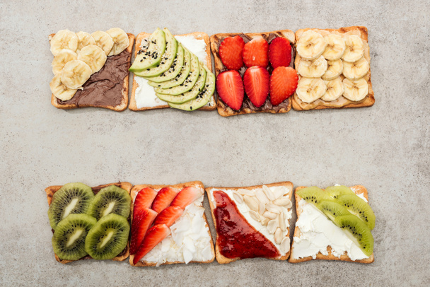 Top view of toasts with cut fruits, berries and peanuts on textured surface - Zdjęcie, obraz