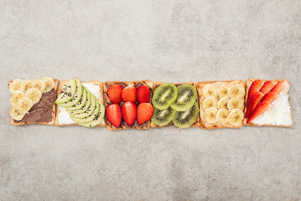 Top view of toasts with cut fruits and berries on textured surface - Photo, Image