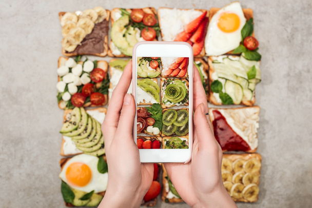 Részleges kilátás smartphone és bevétel fénykép pirítós, gyümölcs és zöldség nő - Fotó, kép