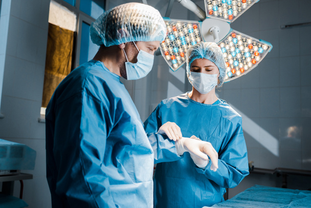 nurse in uniform and medical mask putting latex glove on hand of doctor  - Photo, Image