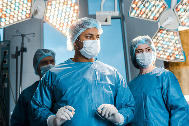 médicos y enfermeras en uniformes y máscaras médicas mirando hacia otro lado en el quirófano
 - Foto, imagen