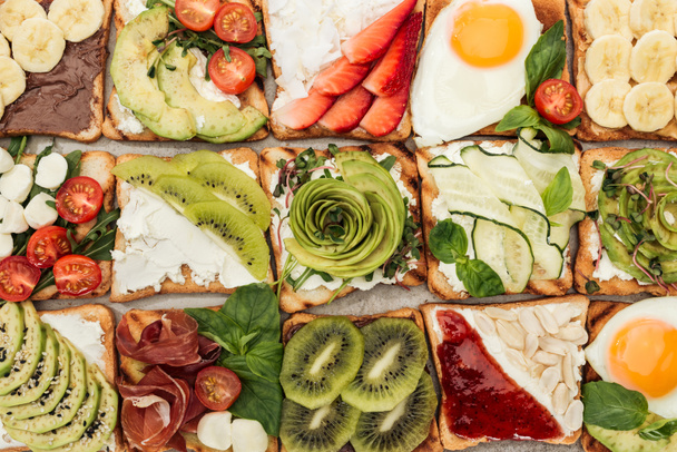 Top view of toasts with fried eggs, cut vegetables and fruits on textured surface - Фото, зображення