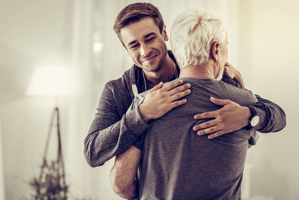 Smiling handsome young man embracing grey-haired dad cheering him up - Photo, Image