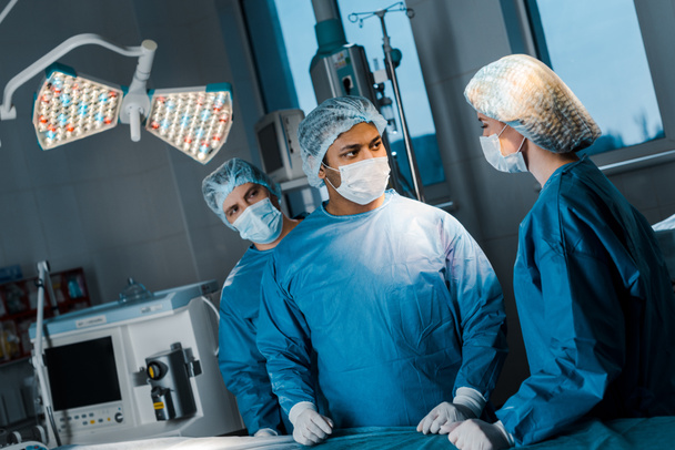 лікарі і медсестра в уніформі і медичні маски розмовляють в операційній кімнаті
 - Фото, зображення
