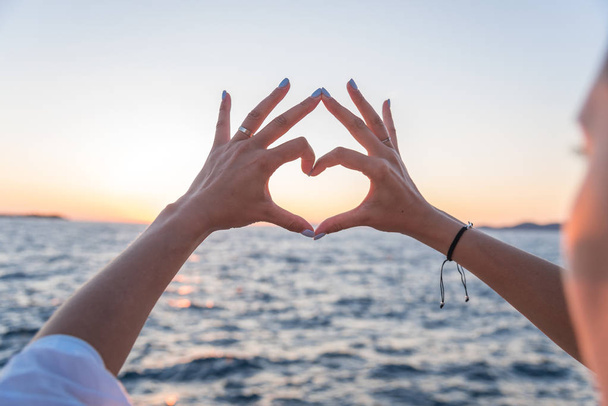 Young female beautiful hands on the background of the sea show the symbol of the heart. Vacation - concept. - Foto, Imagen