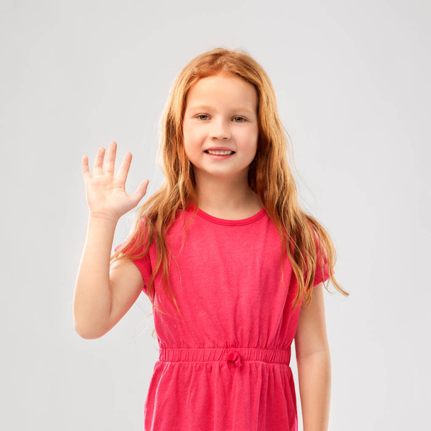smiling red haired girl in pink dress waving hand - Foto, Imagem