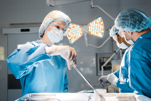 médicos haciendo operación y enfermera en uniforme y equipo de retención de gorra médica
  - Foto, Imagen