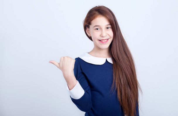 Portrait of a smiling girl pointing her finger to the side on a light background. Schoolgirl. - Foto, Imagem