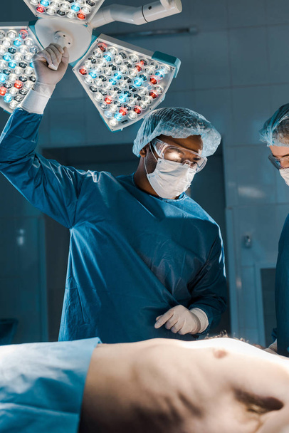 médico y enfermero en uniformes y gorras médicas mirando al paciente en quirófano
  - Foto, Imagen