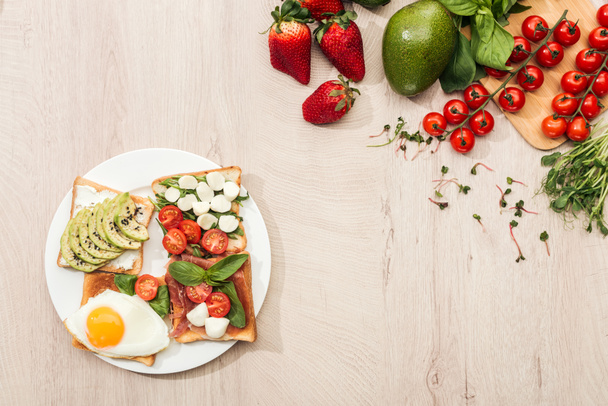 top view of delicious toasts with vegetables on plate and fresh ingredients on wooden table - Φωτογραφία, εικόνα