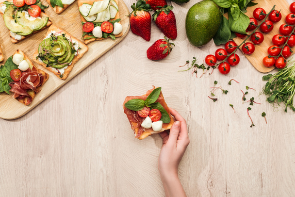 top view of woman with delicious vegetable toasts and fresh ingredients on wooden table - Photo, Image