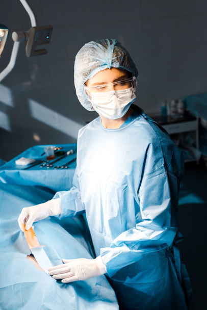 enfermera en uniforme y gorra médica que se pone en tira en quirófano
 - Foto, imagen