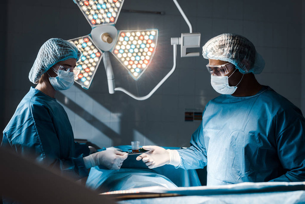 enfermero en uniforme y gorra médica dando equipo médico al cirujano
  - Foto, Imagen