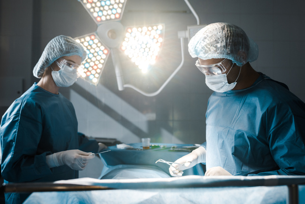 Cirujano y enfermera en uniformes y gorras médicas haciendo operación
  - Foto, Imagen