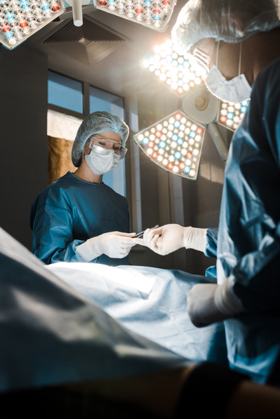 enfoque selectivo de la enfermera en uniforme y gorra médica dando equipo médico al cirujano
  - Foto, imagen
