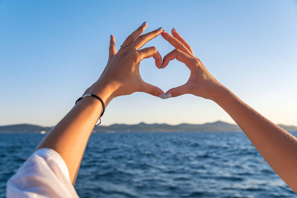 Fiatal nő gyönyörű kezek, a háttérben a tenger mutatják a szív szimbólum. Nyaralás - koncepció. - Fotó, kép
