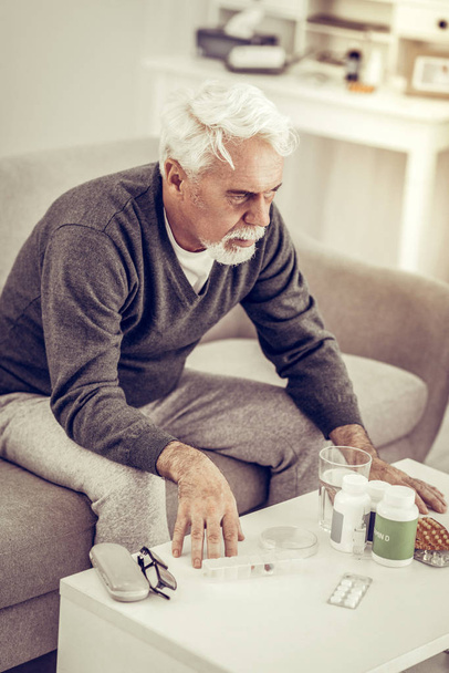 Elderly man sitting at table full of pills boxes - Photo, image