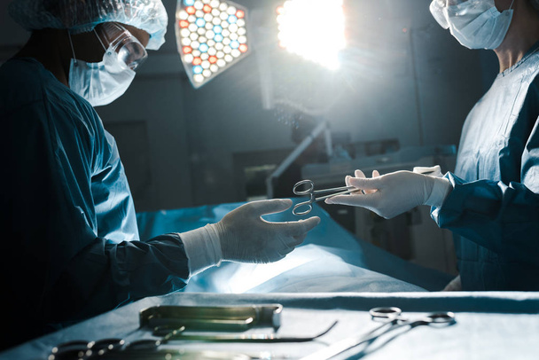ošetřovatelka v uniformě a lékařská maska poskytující lékařské vybavení chirurgovi  - Fotografie, Obrázek