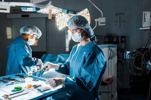 cirurgião fazendo operação e enfermeira segurando tampão na sala de cirurgia
  - Foto, Imagem