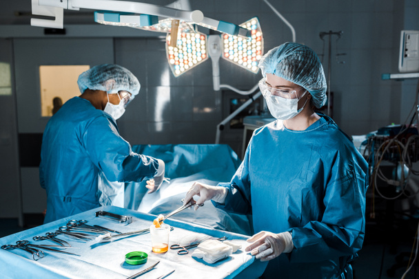 Chirurg wykonuje operację i pielęgniarka w mundurze trzymania tampon w sali operacyjnej  - Zdjęcie, obraz