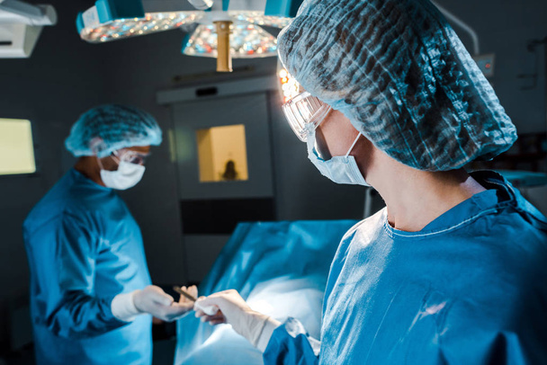 selektiver Fokus der Krankenschwester, die dem Chirurgen im Operationssaal medizinische Geräte zur Verfügung stellt  - Foto, Bild