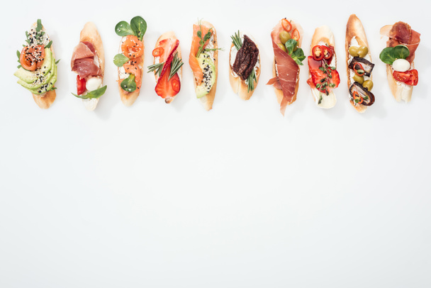 top view of traditional italian bruschetta with prosciutto, salmon, fruits, vegetables and herbs on white with copy space - Photo, Image
