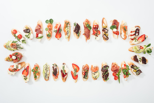 top view of arranged italian bruschetta with prosciutto, salmon, fruits, vegetables and herbs on white - Photo, Image