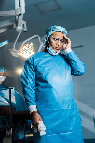enfoque selectivo del médico en uniforme y máscara médica mirando hacia otro lado en el quirófano
 - Foto, Imagen