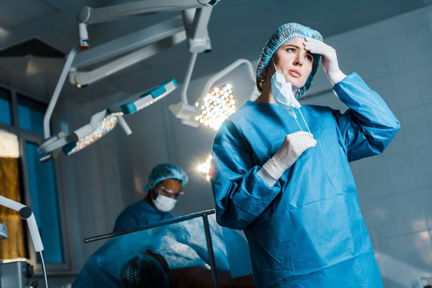 επιλεκτική εστίαση της νοσοκόμας στην ομοιόμορφη βάζοντας την ιατρική μάσκα στο χειρουργείο - Φωτογραφία, εικόνα