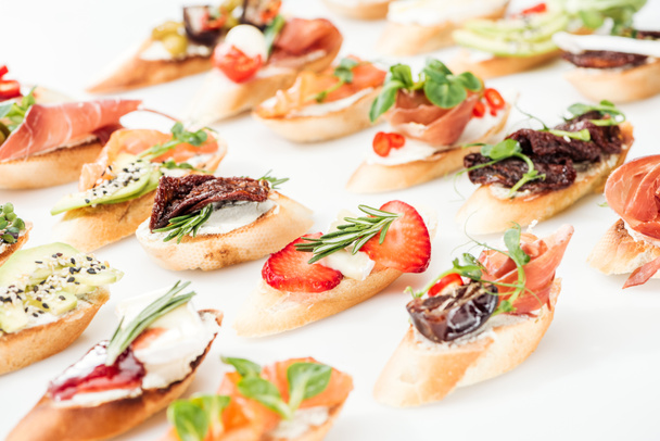 selective focus of italian bruschetta with dried tomatoes, prosciutto, avocado, strawberries and herbs - Photo, Image