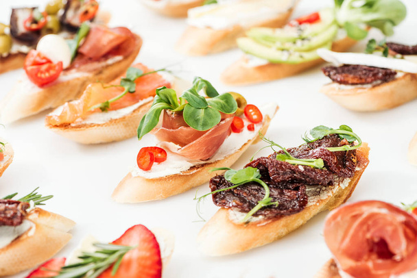 selective focus of italian bruschetta with dried tomatoes, prosciutto, salmon and herbs on white - Foto, imagen