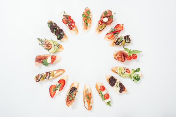 top view of round frame made of traditional italian bruschetta with salmon, prosciutto, herbs and various fruits with vegetables - Photo, Image