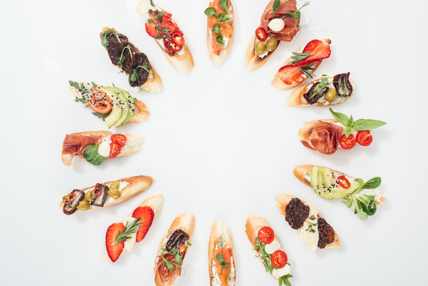 vista superior de marco redondo hecho de bruschetta italiana tradicional con salmón, jamón, hierbas y varias frutas con verduras
 - Foto, Imagen