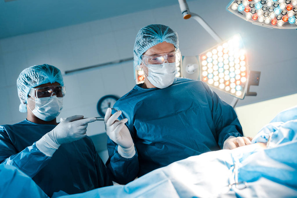 νοσοκόμα με στολή και ιατρική μάσκα δίνοντας ιατρικό εξοπλισμό σε χειρουργό  - Φωτογραφία, εικόνα
