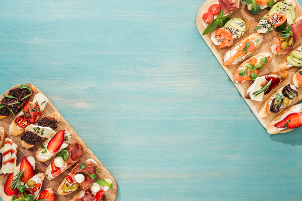 top view of italian bruschetta with prosciutto, salmon and herbs on chopping boards with copy space - Фото, изображение