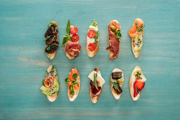 top view of italian bruschetta with salmon, dried tomatoes, prosciutto and herbs on wooden table - Fotoğraf, Görsel