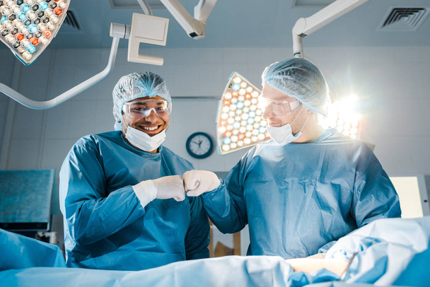 nurse and surgeon in uniforms doing gesture and smiling in operating room  - Photo, Image