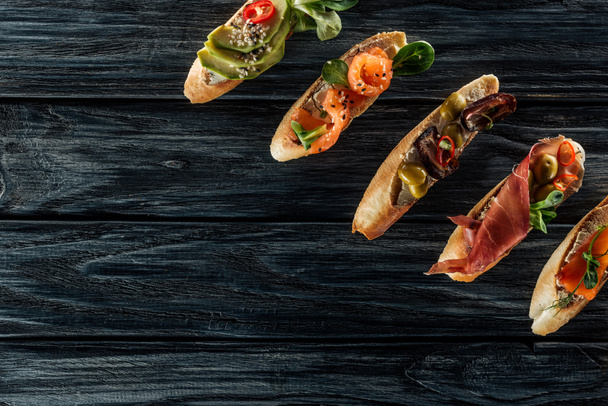 top view of italian bruschetta with salmon, prosciutto and olives on wooden table - Fotó, kép