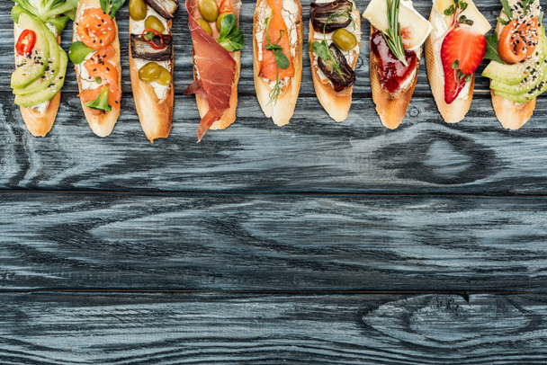 top view of italian bruschetta with prosciutto, herbs, salmon and vegetables on wooden table with copy space - Zdjęcie, obraz