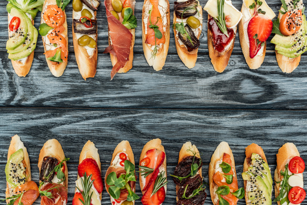 top view of italian bruschetta with prosciutto, herbs, salmon and vegetables on wooden table - Фото, зображення