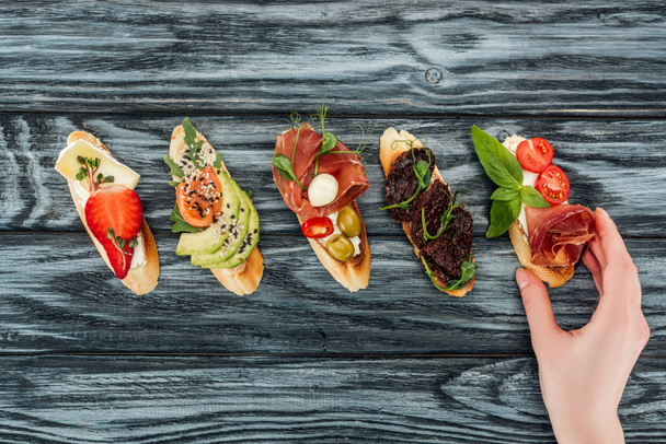 cropped view of woman and italian bruschetta with prosciutto, salmon and vegetables on wooden table - Фото, зображення
