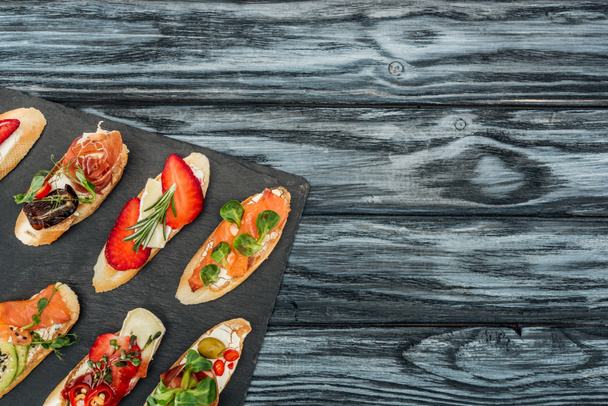top view of italian bruschetta with strawberries, salmon and prosciutto on chopping board with copy space - Фото, изображение