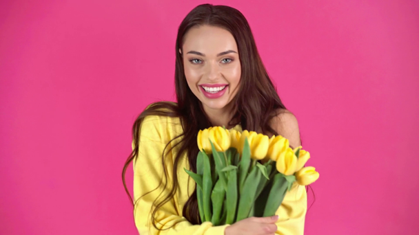 studio shoot of happy young woman turning around with yellow tulips and smelling flowers on crimson background - Footage, Video