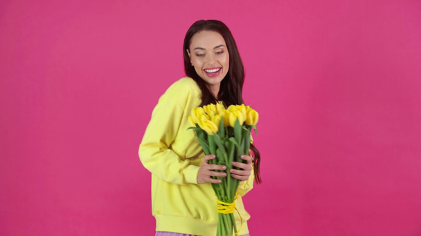 studio shoot of happy young woman smelling yellow tulips and dancing on crimson background - Footage, Video