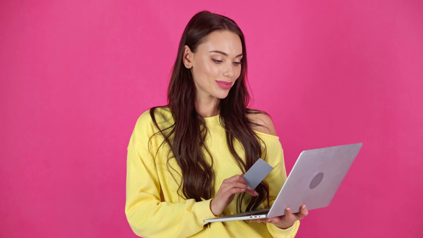 студийная съемка привлекательной улыбающейся молодой женщины с кредиткой и ноутбуком на малиновом фоне
 - Кадры, видео