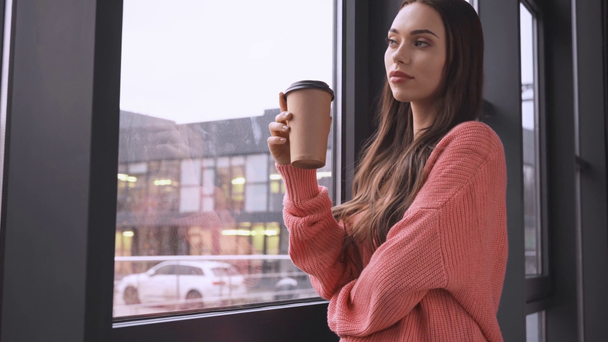 gyönyörű álmodozó fiatal nő néz ki az ablak, és iszik kávé papírpohár - Felvétel, videó
