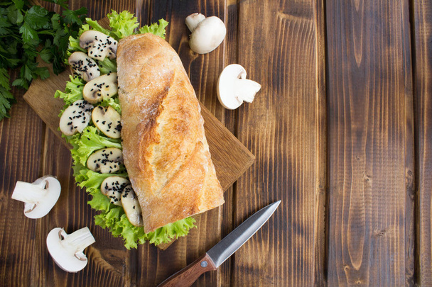 Вегетарианский сэндвич с шампиньонами, листьями летучей мыши и черной сеткой на разделочной доске на коричневом деревянном фоне.
. - Фото, изображение