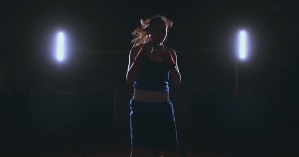 Op zoek naar de camera een mooie vrouwelijke bokser stakingen tegen een donkere achtergrond met een licht verlicht. Steadicam schot - Video